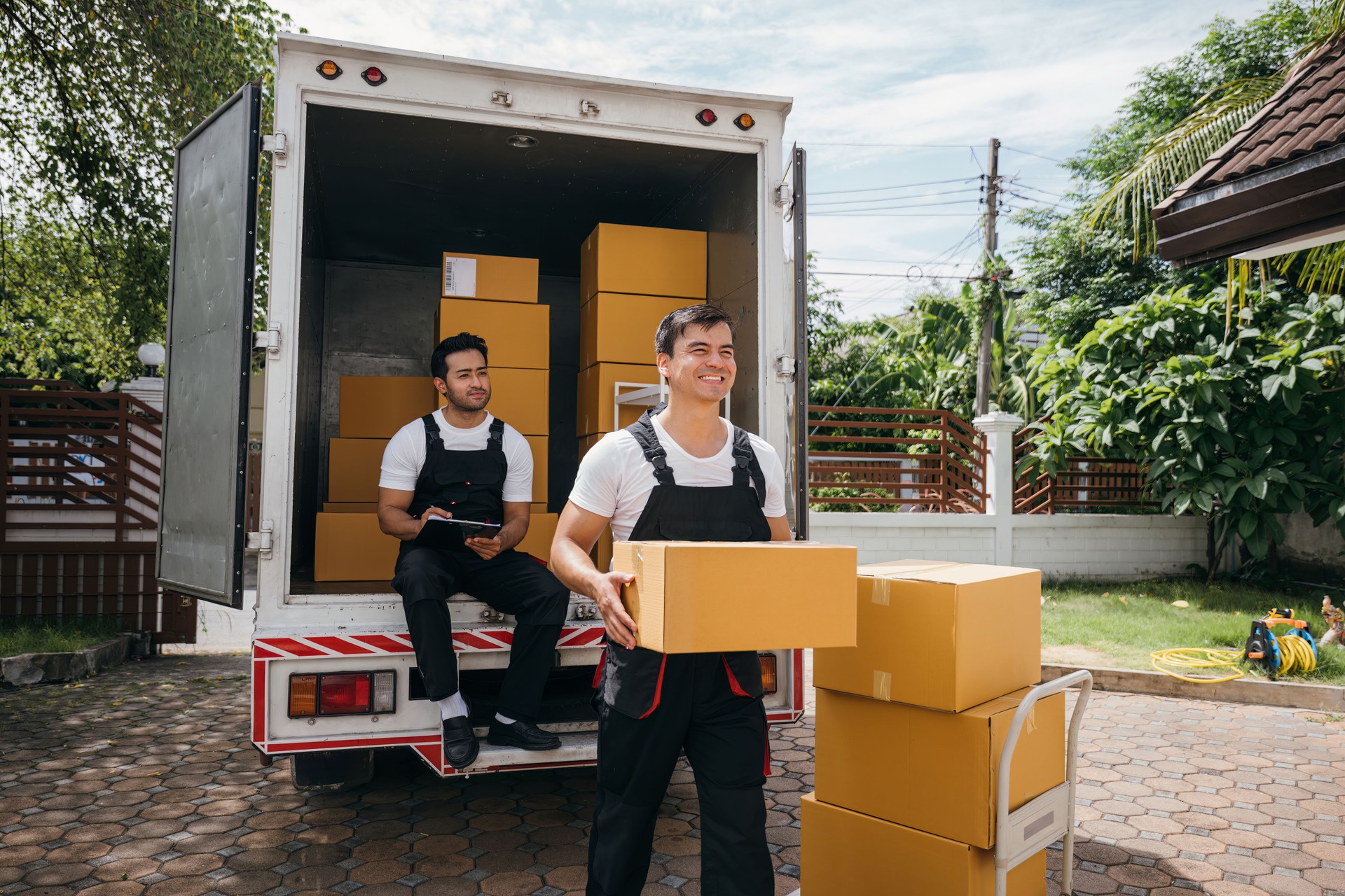 Moving service workers unload boxes from a van showing teamwork and cooperation. Delivery men in uniform relocating items. Smiling employees carrying orders. relocation teamwork Moving Day