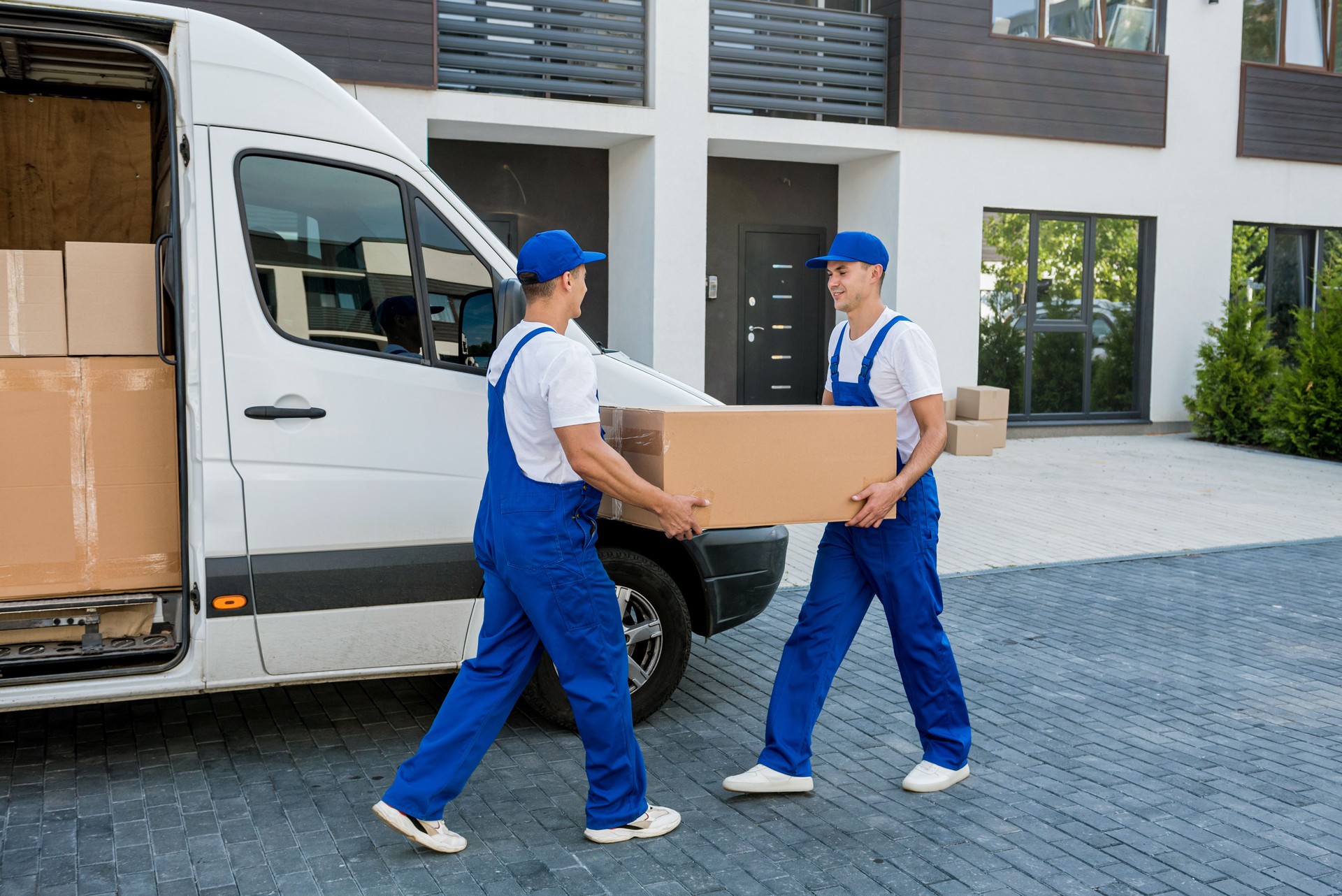 Two removal company workers unloading boxes from minibus into new home